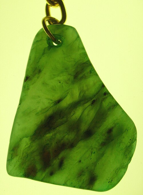 Thin cut green nephrite carving, on hook, showing natural fissures and black specks